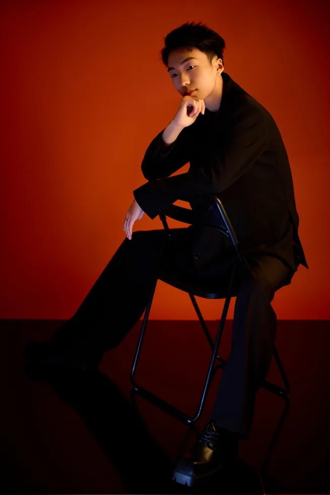 Seated black suit portrait of ZGY against red